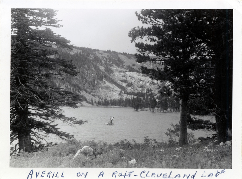 Two people paddle a raft on a lake. A section of a mountain is visible in the background. "Averill on a raft- Cleveland Lake" is written on the front of the photo. The number 217 is stamped on the back of the photograph.