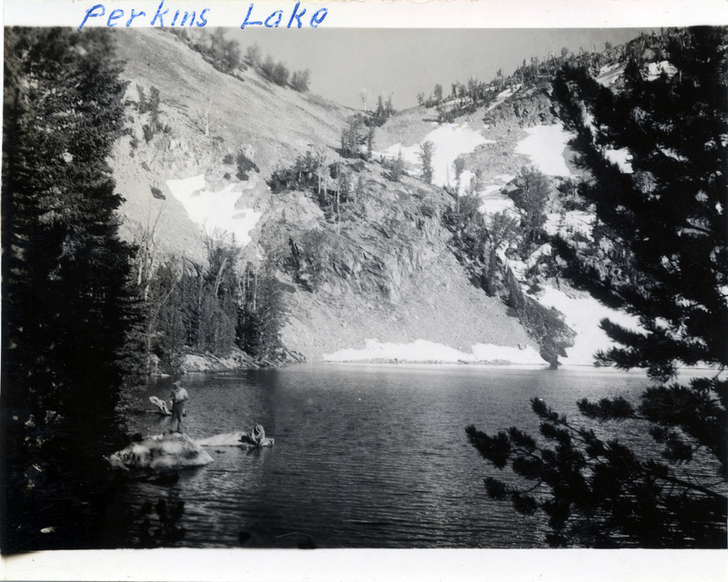 Two people stand on rocks in a lake. "Perkins Lake" is written on the front of the photograph.