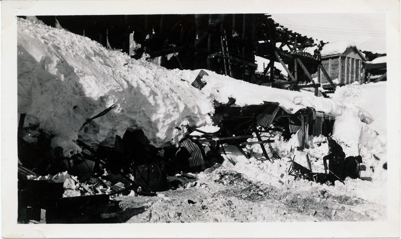 Two people dig next to a building which has been crushed by snow. The back of the photo is stamped with the number 16.