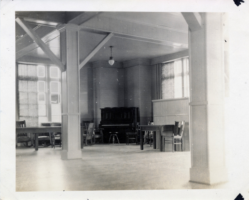 A classroom with a piano, tables, and chairs.