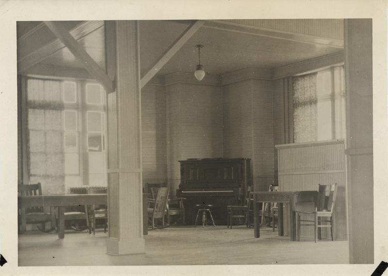 A classroom with a piano, tables, and chairs.