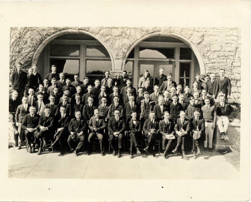 A large group of men pose together in front of a stone building.