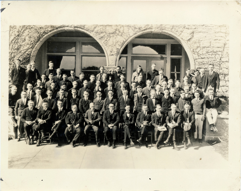 A large group of men pose together in front of a stone building.