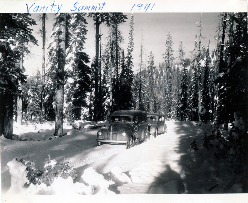 People drive two automobiles over a snowy forest road. "Vanity Summit 1941" is written on the photograph. The back of the photograph is stamped with the number 14.