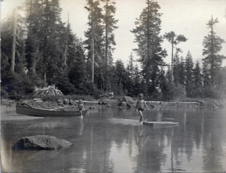 Two children stand in a lake. One is next to a canoe. On the back of the photo is written: " Carol & Vernice, Summit Lake Aug 1934."