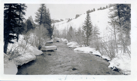 A river moves through a snowy landscape. There are ink marks on the front of the photograph. "Wood river above Ketchum Apr 10-38" is written on the back of the photograph.