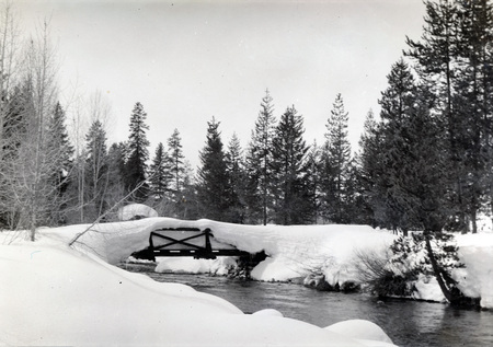 A snow-covered bridge over a stream in a forest area. "Easley Ap 10, 1938" is written on the back of the photograph.