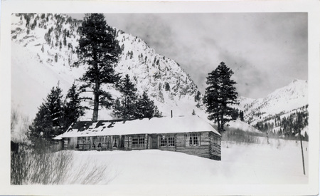 A single-story wooden house at the base of mountains. "4/17/1938 Mascot Mine, Sam Rutherford Author lived there." is written on the back of the photograph.