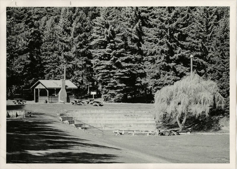 Outdoor recreational area in the Shattuck Arboretum on the University of Idaho campus. Facility includes picnic tables, a building, and a sitting area surrounded by trees. Theatre plays have been staged there. Photo by Leo Ames.