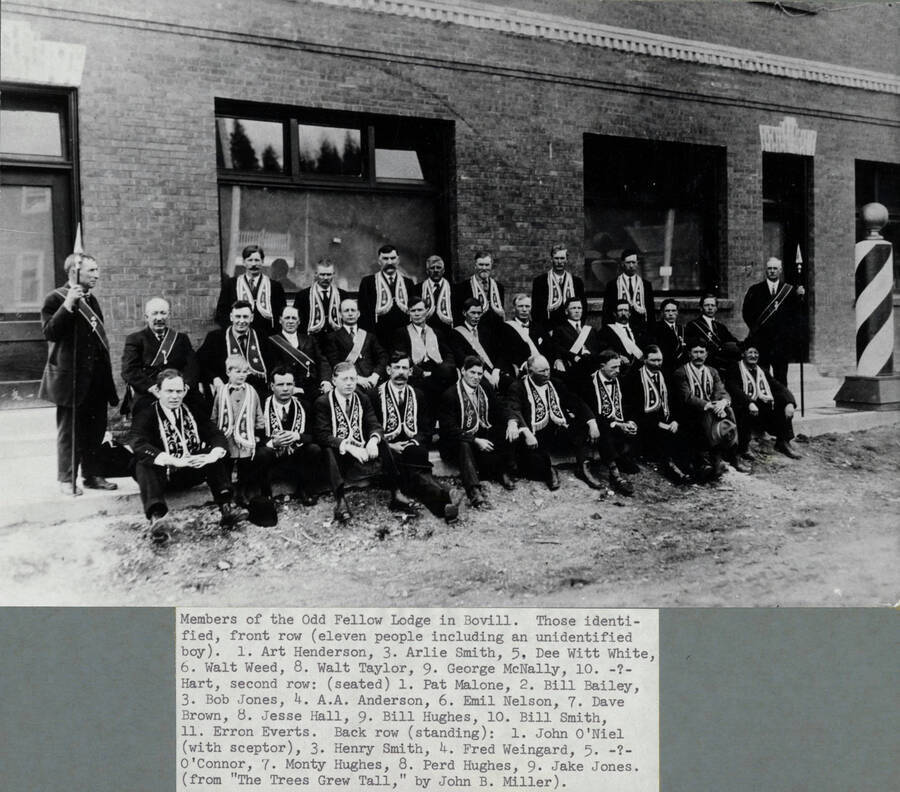 Members are idenitified in caption: 'Members of the Odd Fellow Lodge in Bovill. Those identified, front row (eleven people including an unidentified boy). 1. Art Henderson, 3. Arlie Smith, 5. Dee Witt White, 6. Walt Weed, 8. Walt Taylor, 9. George McNally, 10. -?- Hart, second row: (seated) 1. Pat Malone, 2. Bill Bailey, 3. Bob Jones, 4. A.A. Anderson, 6. Emil Nelson, 7. Dave Brown, 8. Jesse Hall, Bill Hughes, 10. Bill Smith, 11. Erron Everts. Back row (standing): 1. John O'Niel (with sceptor), 3. Henry Smith, 4. Fred Weingard, 5. -?- O'Connor, 7. Monty Hughes, 8. Perd Hughes, 9. Jake Jones.'