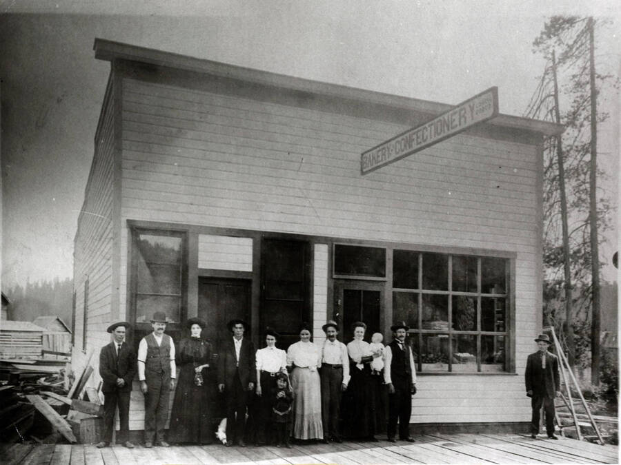 This frame building, which was the original Groh grocery and bakery, burned in 1912. Four people in the line are identified, beginning with the 6th, these are Mrs. Alice Taylor, Mr. Taylor, Alvina Groh holding a baby - possibly Harold Taylor - and John Groh.