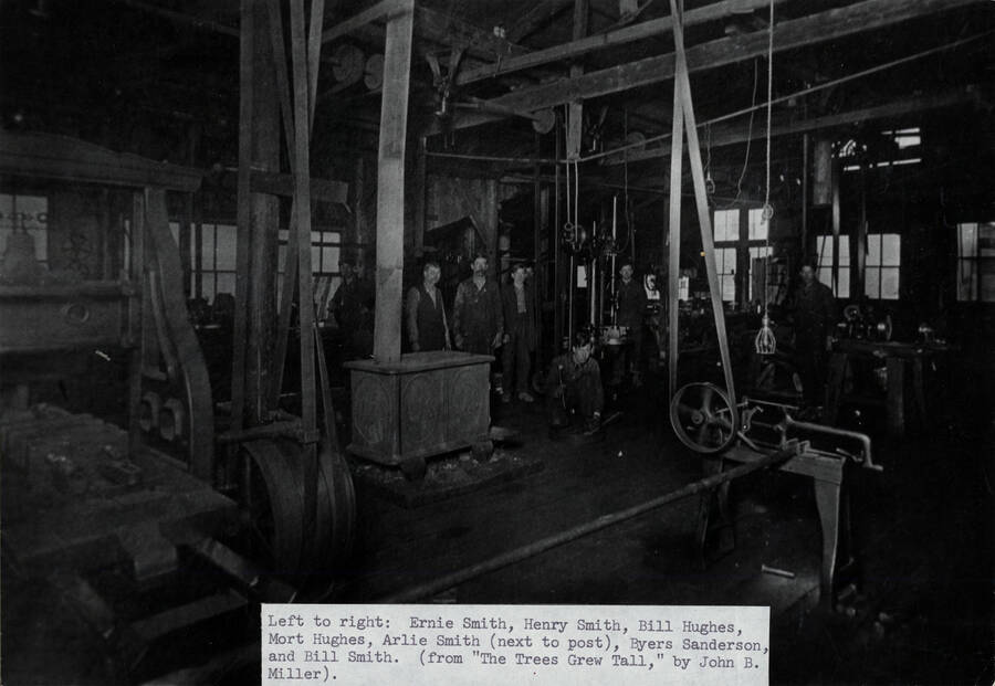 The interior of the machine shop at Potlatch Lumber Company's Camp 8 near Bovill, Idaho. People are identified in caption. Left to right: Ernie Smith, Henry Smith, Bill Hughes, Mort Hughes, Arlie Smith (next to post), Byers Sanderson, and Bill Smith.