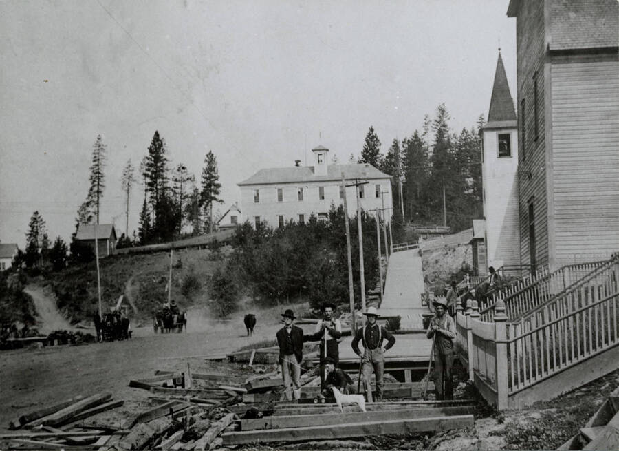 Workers build a wooden sidewalk in Troy, Idaho. The school is in the background.