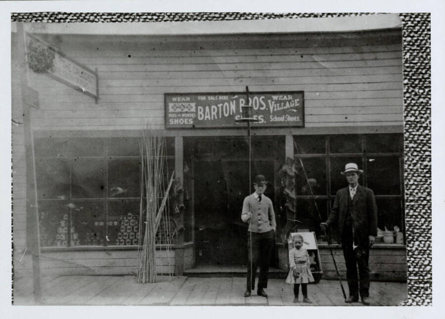Standing in front left to right are Dr. R.T. Witty, a Simmons girl, and Mr. Simmons. Along the wall are a bunch of cane fishing poles and, hanging on the door-jam, are logger's boots. The building also housed the Max Davis Drug Store, whose sign is visible at the upper left: 'M. Davis, druggist - Ready to serve you day and night.' The store was on Main Street just east of First Avenue, where the service station now stands.
