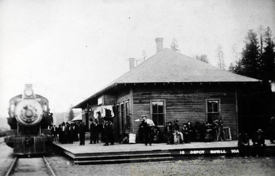 People occupy the platform of the Washington, Idaho & Montana Railway Co. depot in Bovill. A train waits on the tracks in the left of the photo.
