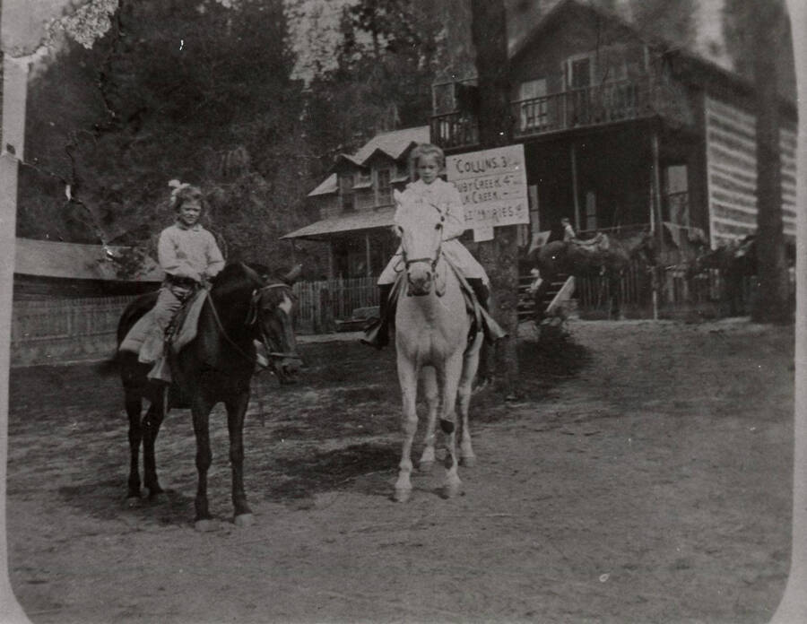 Two young girls sit on horseback  in front of the Bovill Hotel. The girl on the left is thought to be Dorothy Bovill, and the girl on the right is thought to be Gwendolyn Bovill.