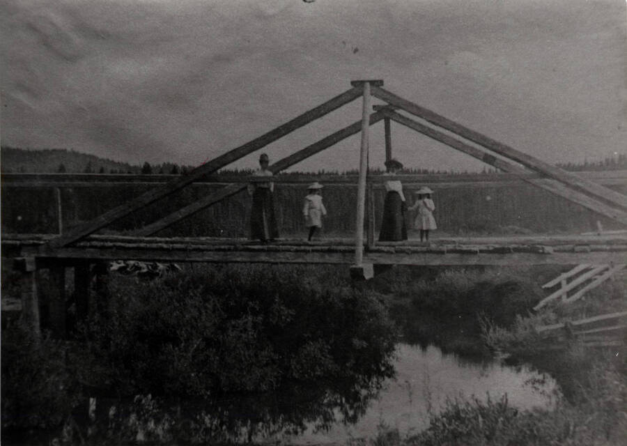Two women and two children stand on a bridge over the Potlatch River.