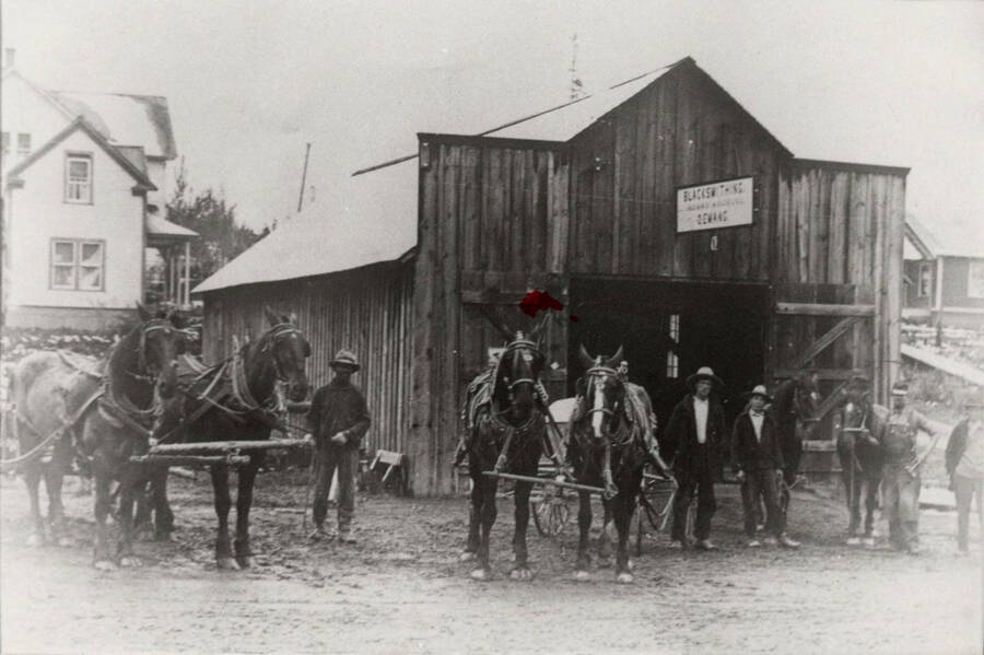 Five unidentified men and two horse teams stand in front of the blacksmith shop in Deary, Idaho.