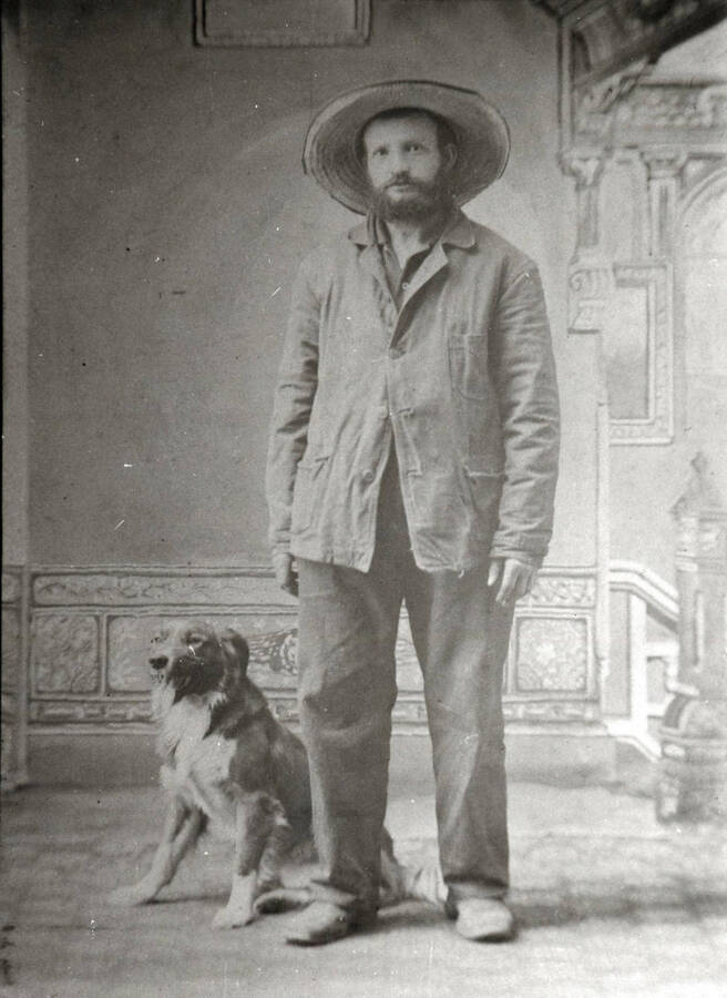Tom Groh as a miner, posed standing with a dog indoors.