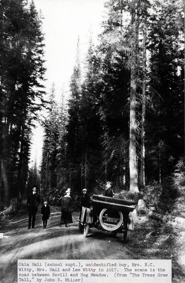 From left to right: School Superintendent Okia Hall, unidentified boy, Gertrude Hale Witty, Mrs. Hall, Lee Witty. The scene is the road between Bovill and Hog Meadow. The automobile appears to be a 1916 Ford Model T Touring car.