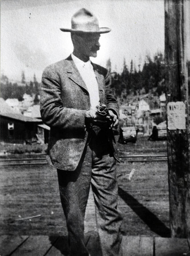 Hugh Bovill stands on a wooden sidewalk in Troy, Idaho. The post picture on his right has a wanted poster fixed to it.