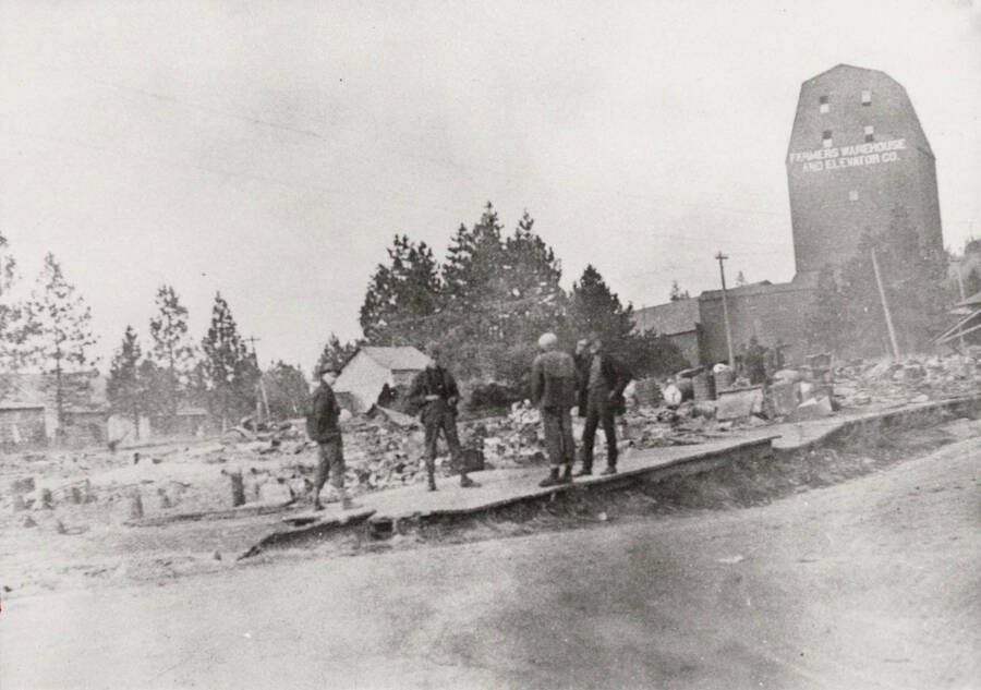 Aftermath of a fire in Deary, Idaho in 1905. Four unidentified people stand atop rubble in the foreground.