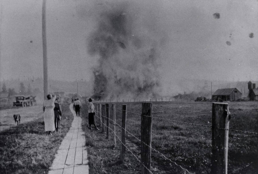 From Trees Grew Tall: 'More than 75,000 cedar posts go up in flames in the southwest part of the cedar yard. This one, in 1920, was the only serious fire ever to occur in the yard. Rails on track 1 were broken by the heat and curled into spirals. The woman in the foreground is Mrs. Ellison.'