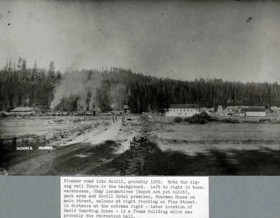 Pioneer road into Bovill, probably 1909. Note the zig-zag rail fence in the background. Left to right in town: warehouses, Shay locomotives (depot not yet built), park area and Bovill Hotel premises, Sherman House on main street, saloons at right fronting on Pine Street. In the distance at extreme right - later location of David Boarding House - is a frame which was probably the recreation hall.