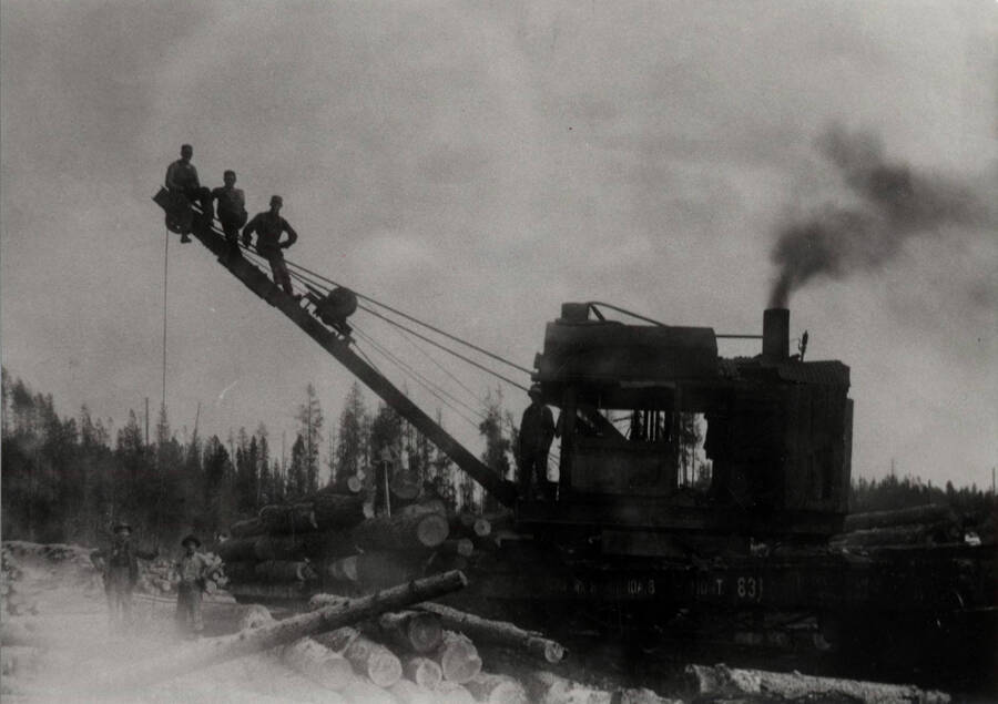 A Marion steam log loader with three crew members sitting on the boom.