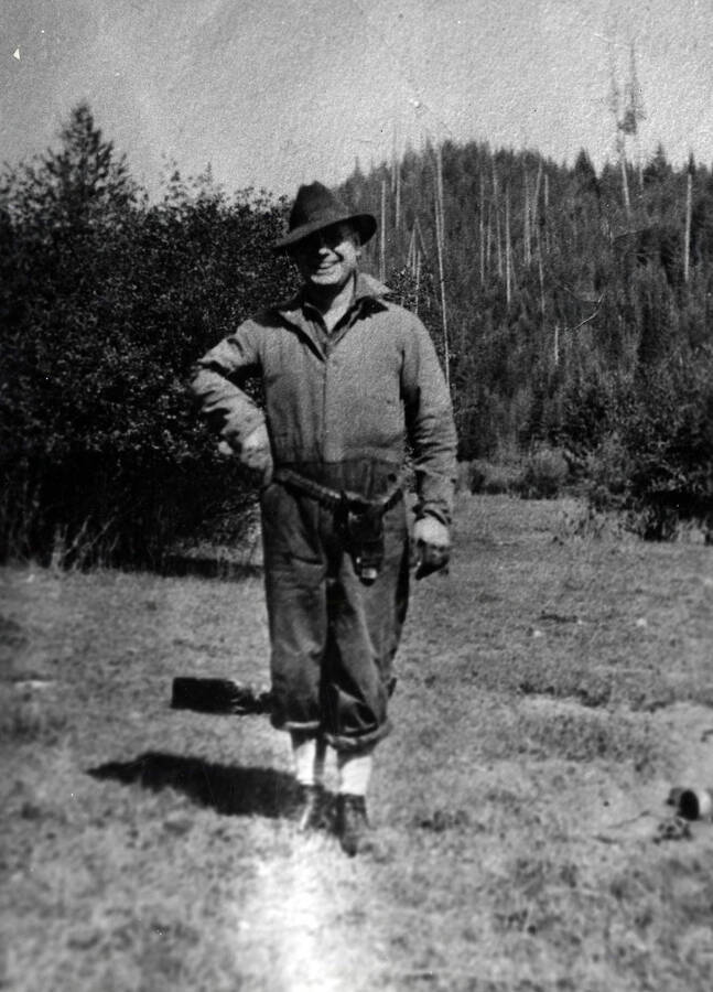 Dr. F.C. Gibson is here shown standing along a trail with one hand on his pistol belt.