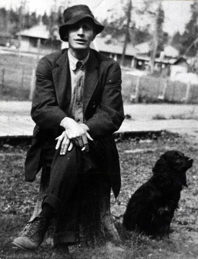 Dr. Will Young seated on a stump, a dog at his left.