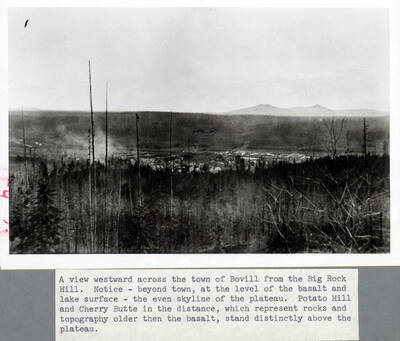 A view from east of Bovill from the vantage point of Big Rock Hill, looking west. Bovill itself is framed in the middle ground with forests on each side. Cherry Butte and Potato Hill are visible in the distance.