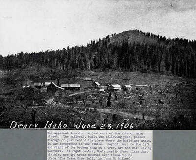 The apparent location is just east of the site of main street. The railroad, built the following year, passed through or just behind the place where the buildings stand. In the foreground is the stable. Beyond, seen to the left and right of the broken snag of a tree, are the main living quarters. At right center, their partly drawn flaps just visible, are two tents mounted over frame floors.