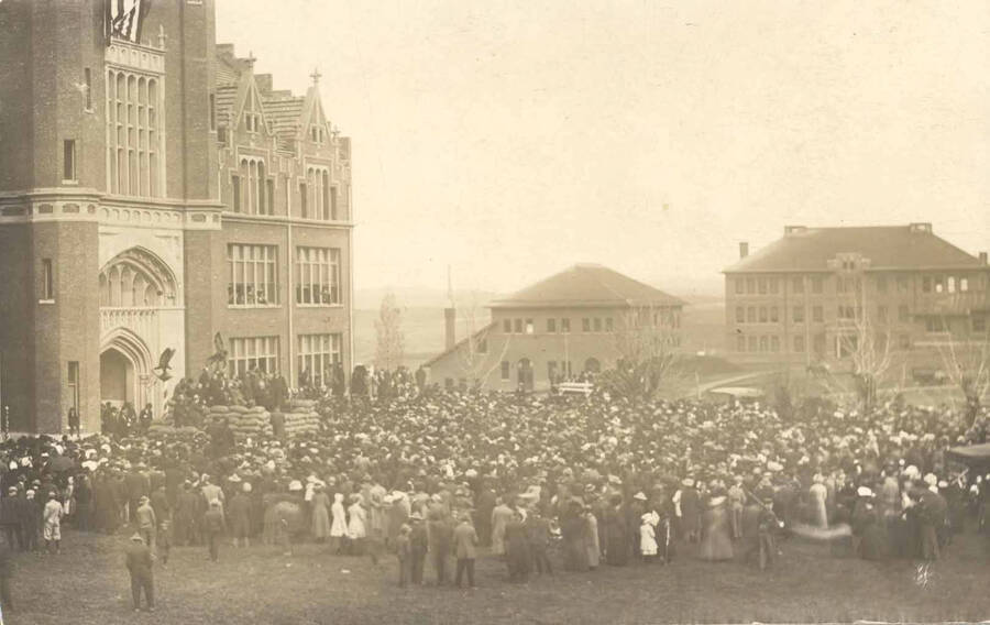 Theodore Roosevelt speaks from a platform made of sacks of wheat in front of University of Idaho Administration Building. His right arm is raised.