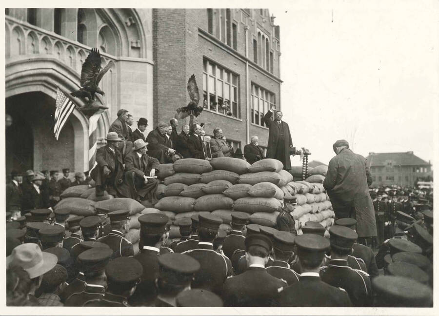 Theodore Roosevelt speaking on platform in front of University of Idaho Administration Building, his right arm is raised up.