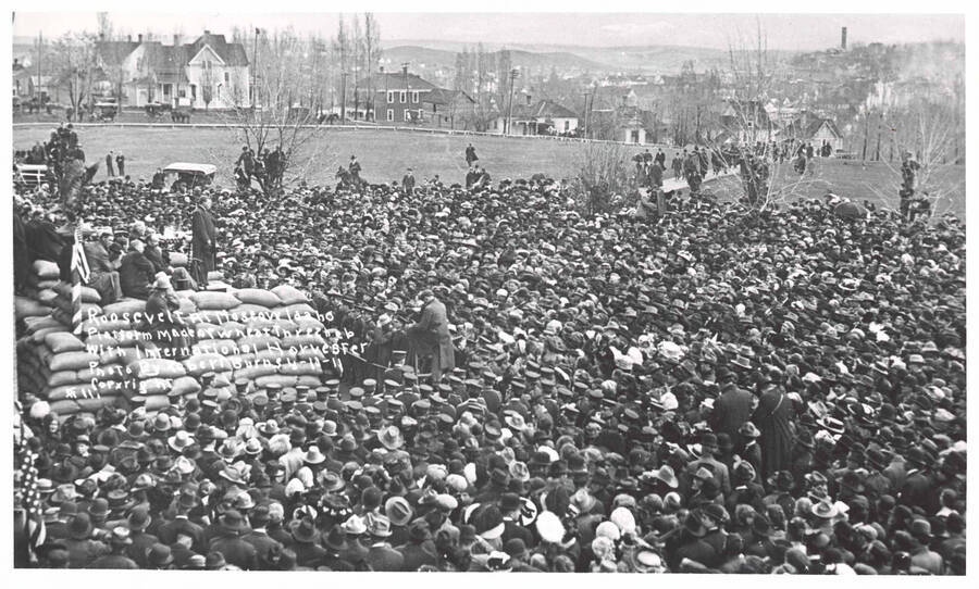Crowd assembled on University of Idaho campus to hear Theodore Roosevelt speak. Writing on image reads: 'Roosevelt at Moscow Idaho Platform made of wheat threshed with International Harvester. Photo by Robert Burns 4-10-11 Copyright #11.'