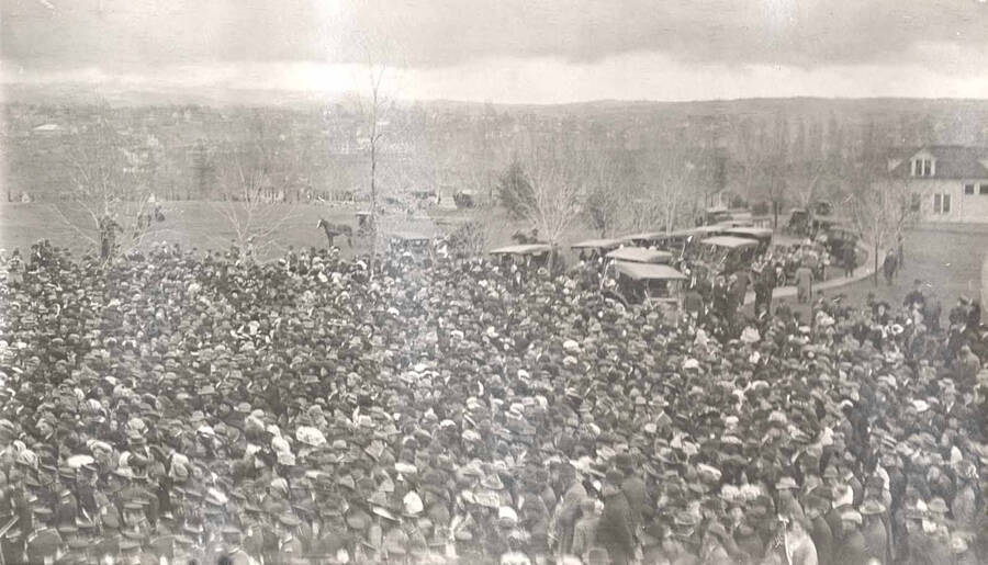 The crowd assembled on University of Idaho campus to hear Theodore Roosevelt speak. Roosevelt is visible, arm outstretched, on the platform on the left side of the photograph.
