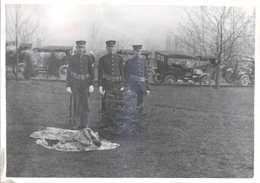 Three uniformed men standing behind the tree planted by Theodore Roosevelt.