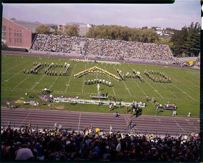 Marching band, cheerleaders and flag squad performing on football field, formations include spelling out the word Idaho and various geometric shapes.