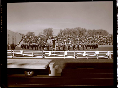 Marching band, cheerleaders and flag squad performing on football field.