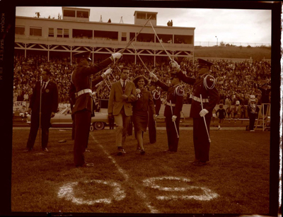 Marching Band, cheerleaders, and spectators at football game at Neale Stadium, includes image of historic Vandal mascot.
