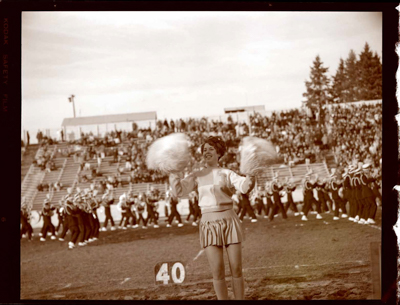 Marching Band, cheerleaders, pep squad, and spectators at football game in Neale Stadium.