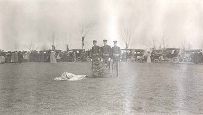 Three uniformed men standing behind the tree planted by Theodore Roosevelt.