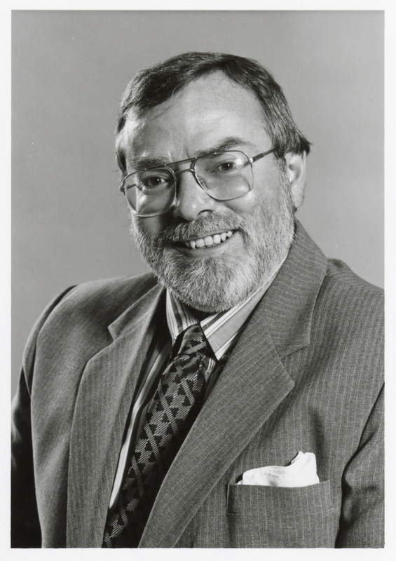 Black and white photograph of a person wearing a suit and glasses.