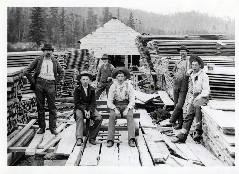 A.W. Post and crew stand  in the Company yard and sawmill, Rathdrum, Idaho. A.W. Post is in the back 3rd from left. John W. Post is in the front 4th from left. Courtesy of Mrs. John Post, Coeur d'Alene, Idaho.