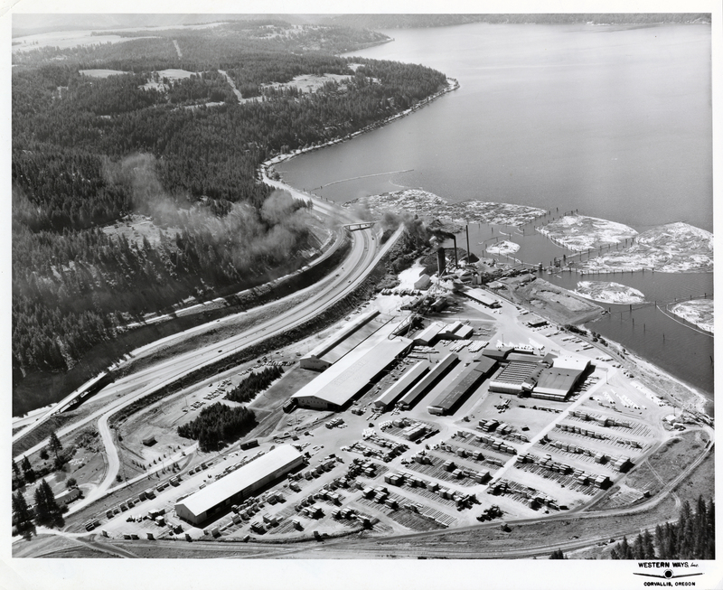 Aerial view of PFI's (Potlatch Forests Incorporated) Rutledge Unit yard, Coeur d'Alene, Idaho. Credit to Western Ways Incorporated. Roof of largest building reads: 'Coeur D'Alene'. Side of connected building reads: 'Safety everywhere all the time'. Courtesy of the Rutledge Unit.
