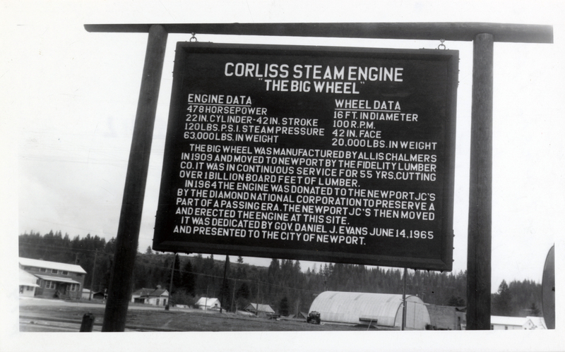 Corliss Steam Engine sign in Newport, Washington. Sign reads as follows: 'Corliss Steam Engine 'The Big Wheel'. Engine Data- 478 Horsepower, 22 inch cylinder-42 inch stroke, 120 pounds P.S.I. steam pressure, 63,000 pounds in weight. Wheel data- 16 feet in diameter, 100 R.P.M., 42 inch face, 20,000 pounds in weight. The Big Wheel was manufactured by Aliss Chalmers in 1909 and moved to Newport by the Fidelity Lumber Company. It was in continuous service for 55 years, cutting over 1 billion board feet of lumber. In 1964 the engine was donated to the Newport JC's by the Diamond National Corporation to preserve a part of a passing era. The Newport JC's then moved and erected the engine at this site. It was dedicated by Governor Daniel J. Evans June 14, 1965 and presented to the city of Newport.'