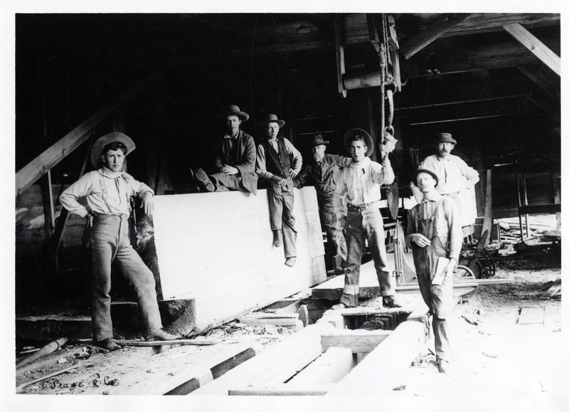 A.W. Post and crew stand in the interior of the sawmill, Rathdrum, Idaho. A.W. Post is in the back 4th from left and John W. Post is in the front first on the left. Courtesy of Mrs. John Post, Coeur d'Alene, Idaho.
