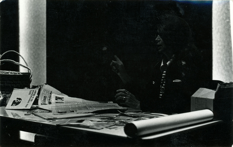 Mariam Moos at a desk covered in newspapers.