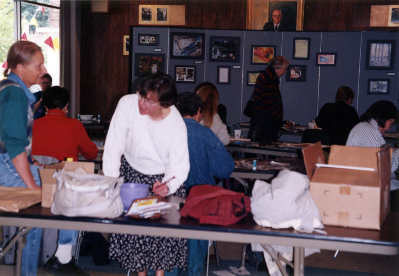 Carol Andreas and Jill Brown at what appears to be an art event. Several women are visible in the background, along with matted artwork displayed on temporary walls.